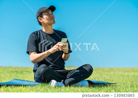 Asian man in sportswear sitting on the grass in the park and using his smartphone 130983865