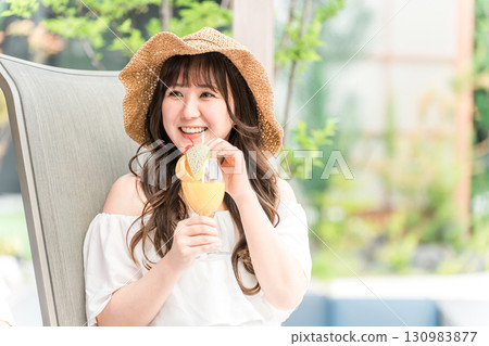 Young Asian woman sitting on a recliner by the pool and drinking tropical juice 130983877