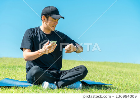 Middle-aged man in sportswear doing yoga, stretching and health care using smart watch and smart band 130984009