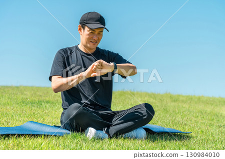Middle-aged man in sportswear doing yoga, stretching and health care using smart watch and smart band Middle-aged man in sportswear doing yoga, stretching and health care using smart watch and smart band 130984010