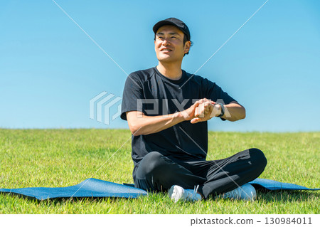 Middle-aged man in sportswear doing yoga, stretching and health care using smart watch and smart band Middle-aged man in sportswear doing yoga, stretching and health care using smart watch and smart band 130984011