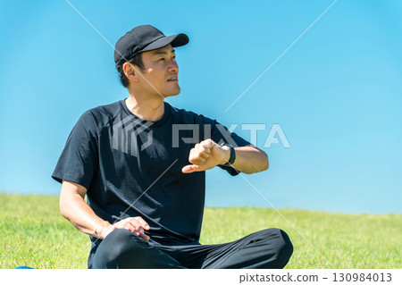 Middle-aged man in sportswear doing yoga, stretching and health care using smart watch and smart band 130984013