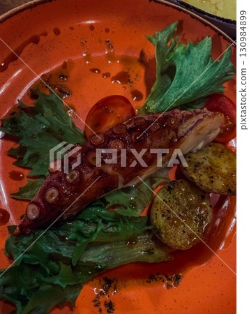 Fried octopus with potatoes and fresh herbs on an orange plate. 130984899