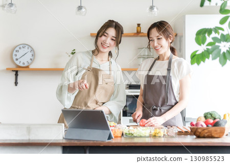 A woman cooking in the kitchen while looking at a tablet (online cooking class, distribution) A woman cooking in the kitchen while looking at a tablet (online cooking class, distribution) 130985523