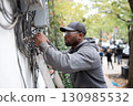 African American electrician in safety glasses laying wires outside a building on a city street 130985532
