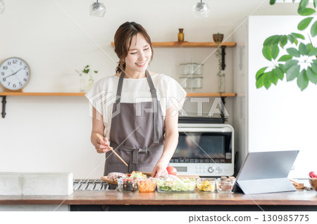 A woman in an apron cooking while looking at a recipe using an app on a tablet A woman in an apron cooking while looking at a recipe using an app on a tablet 130985775