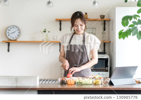 A woman in an apron cooking while looking at a recipe using an app on a tablet A woman in an apron cooking while looking at a recipe using an app on a tablet 130985776