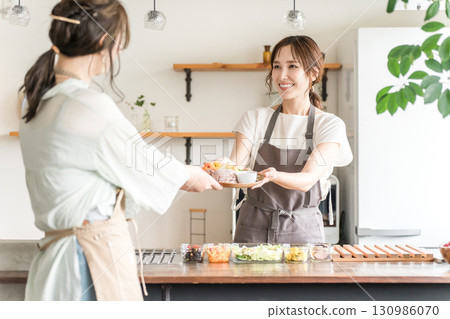 亞洲女咖啡館服務生穿著圍裙從廚房流理台遞上食物 130986070