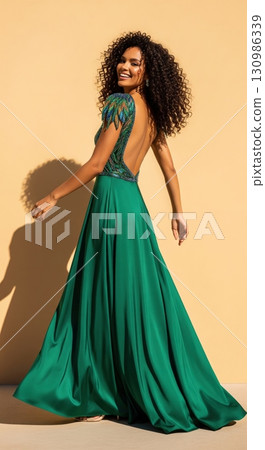 Happy beautiful woman with long curly hair in a green evening gown looking back and smiling 130986339