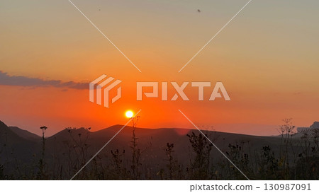 A beautiful sunset in the mountains, with green grass in the foreground. 130987091