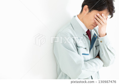 A middle-aged male businessman in work clothes who is worried and covering his face 130987476