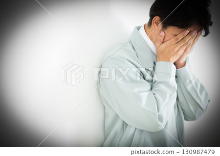 A middle-aged male businessman in work clothes who is worried and covering his face 130987479