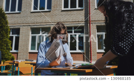 Two high school students collaborating on a project outdoors, embracing the sunshine and fresh air at their school 130988185