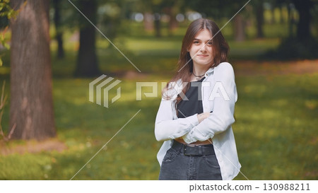 Young georgian woman standing with crossed arms, radiating confidence amid verdant urban greenery and peaceful surroundings Young georgian woman standing with crossed arms, radiating confidence amid verdant urban greenery and peaceful surroundings 130988211