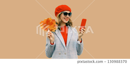 Autumn portrait stylish happy smiling young woman with phone, beautiful girl holding yellow leaves 130988370