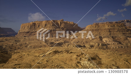 Vast rocky formations rise from the sandy terrain, showcasing the rugged beauty of a remote desert. The clear blue sky enhances the dramatic scenery in this serene landscape. Vast rocky formations rise from the sandy terrain, showcasing the rugged beauty of a remote desert. The clear blue sky enhances the dramatic scenery in this serene landscape. 130988578