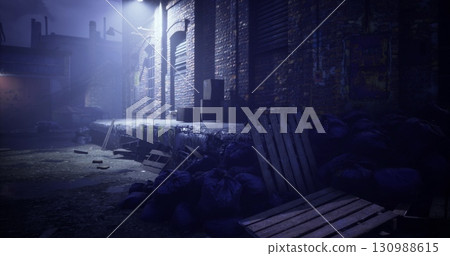 An eerie alleyway is illuminated by a lone streetlight at night. Piles of debris, including wooden pallets and refuse, create a haunting atmosphere in the dimly lit space. An eerie alleyway is illuminated by a lone streetlight at night. Piles of debris, including wooden pallets and refuse, create a haunting atmosphere in the dimly lit space. 130988615