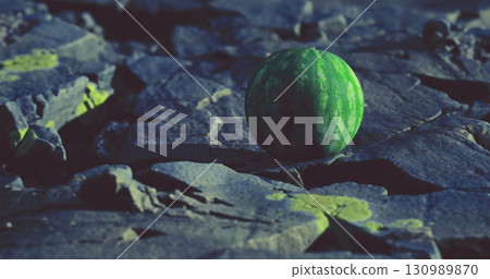A fresh watermelon sits alone on a rugged, dark stone surface, illuminated by soft, moody light. 130989870