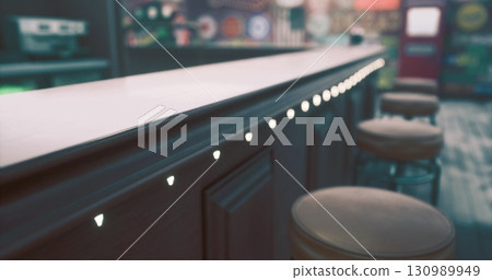 Soft lights highlight the wooden countertop of a vintage bar, inviting customers to unwind. Plush stools are arranged neatly, adorned with a warm, welcoming ambiance that enhances the nostalgic charm. Soft lights highlight the wooden countertop of a vintage bar, inviting customers to unwind. Plush stools are arranged neatly, adorned with a warm, welcoming ambiance that enhances the nostalgic charm. 130989949