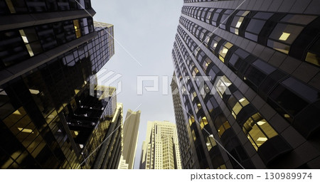 A stunning view of towering skyscrapers reaches towards a pale evening sky. The muted glow from office windows reflects the vibrant energy of a bustling urban environment. 130989974
