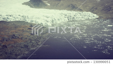 A breathtaking view of a colossal glacier melting into serene, dark waters. Surrounding rocky terrain contrasts beautifully with the icy white expanse as nature unfolds its stunning beauty. A breathtaking view of a colossal glacier melting into serene, dark waters. Surrounding rocky terrain contrasts beautifully with the icy white expanse as nature unfolds its stunning beauty. 130990051
