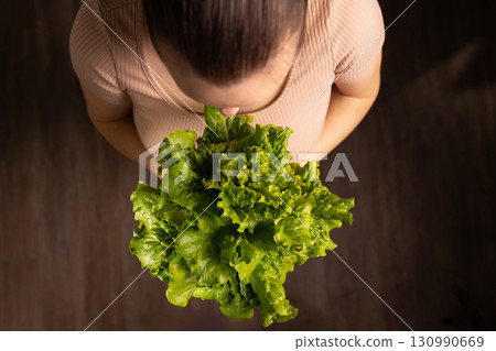 Woman Holds Fresh Green Lettuce in Her Hands While Looking Down at It 130990669