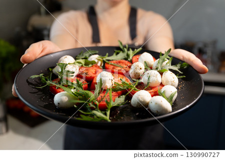 Fresh Salad With Tomatoes, Mozzarella, and Arugula Served on a Black Plate in a Modern Kitchen Fresh Salad With Tomatoes, Mozzarella, and Arugula Served on a Black Plate in a Modern Kitchen 130990727
