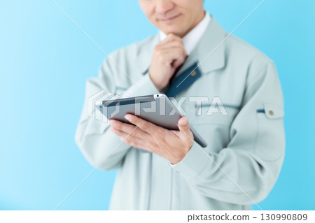 A middle-aged male businessman in work clothes looking at a tablet and worrying A middle-aged male businessman in work clothes looking at a tablet and worrying 130990809