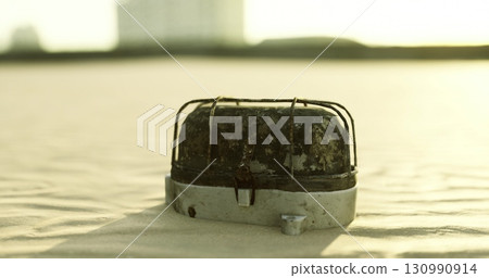 A weathered metal object rests on a shore of fine sand, illuminated by the golden light of the setting sun. The surface shows signs of wear, blending with the tranquil surroundings. A weathered metal object rests on a shore of fine sand, illuminated by the golden light of the setting sun. The surface shows signs of wear, blending with the tranquil surroundings. 130990914