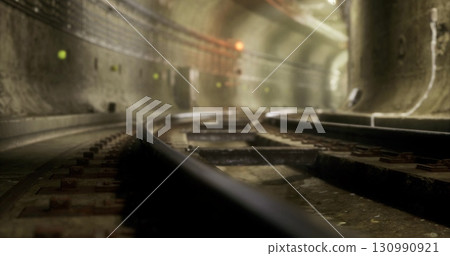 Curved rail tracks stretch into the darkness of a subterranean tunnel, with soft lighting illuminating the walls. The atmosphere feels quiet and isolated, hinting at the bustling activity above. Curved rail tracks stretch into the darkness of a subterranean tunnel, with soft lighting illuminating the walls. The atmosphere feels quiet and isolated, hinting at the bustling activity above. 130990921