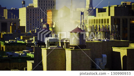 Steam billows from old water towers on rooftops as sunlight casts a warm glow over the city. Skyscrapers outline the skyline in the background, highlighting urban life. 130990933