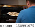 Close-up portrait a cheerful chef working in a pizza place and putting the pizza into the owen. Smiling chef wearing apron uniform and posing. Space for text. 130991075