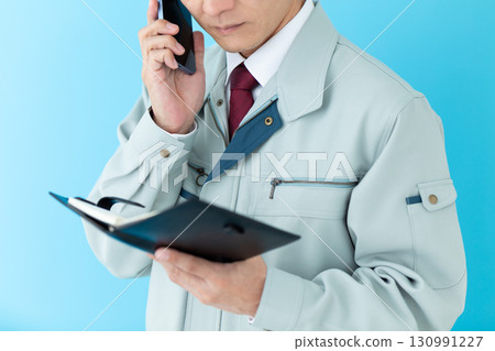一位身穿工作服的中年男性商人一邊看著筆記本,一邊用智慧型手機聊天 一位身穿工作服的中年男性商人一邊看著筆記本,一邊用智慧型手機聊天 130991227