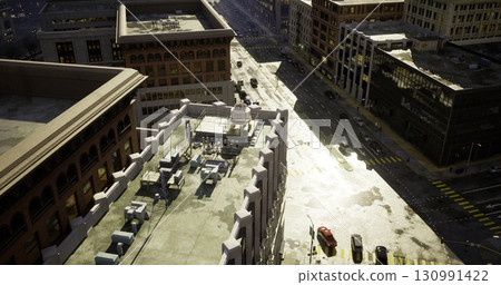 Bright sunlight reflects off the pavement as vehicles navigate a busy urban street. Rooftops are lined with equipment and structures, creating an industrial cityscape. Bright sunlight reflects off the pavement as vehicles navigate a busy urban street. Rooftops are lined with equipment and structures, creating an industrial cityscape. 130991422