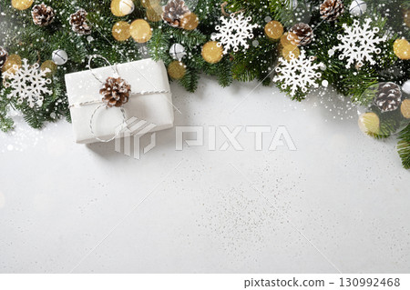 Christmas frame with gift, evergreen branches, snowflakes, pine cones on white background. Copy space. Xmas greeting card. Winter Holiday. View from above. 130992468