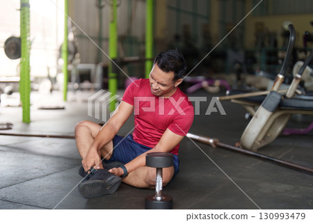 Injury Awareness. Individual sitting on gym floor, holding ankle. 130993479