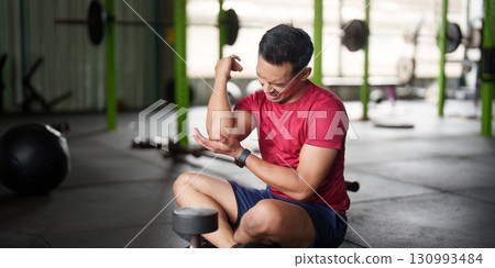 Fitness Injury. Young man feeling elbow pain during weight training in gym. Fitness Injury. Young man feeling elbow pain during weight training in gym. 130993484