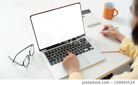 Work from Home. Professional writing notes while using laptop in a cozy workspace. Work from Home. Professional writing notes while using laptop in a cozy workspace. 130993524