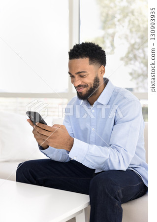 Smiling young male chat on mobile telephone sitting on couch Smiling young male chat on mobile telephone sitting on couch 130993935