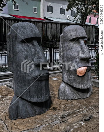 Two Moai statues stand in an urban setting, one making a funny face. Two Moai statues stand in an urban setting, one making a funny face. 130994082