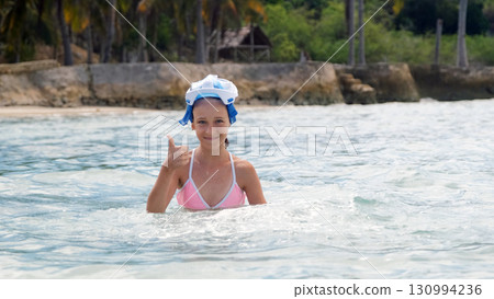 Girl in snorkel mask gives a thumbs up while swimming in bright tropical ocean waters Girl in snorkel mask gives a thumbs up while swimming in bright tropical ocean waters 130994236