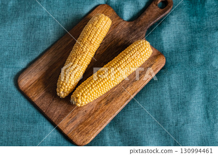 corn a couple of ripe cobs on a wooden cutting board dark brown background corn a couple of ripe cobs on a wooden cutting board dark brown background 130994461