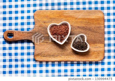 red rice long and black grains in a white plate in the shape of a heart on a wooden background 130994473