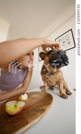 A woman enjoys a fun time with her dog, happily sharing healthy, colorful fruit snacks 130994530