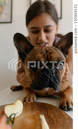 A girl joyfully interacts with her French Bulldog in a cozy kitchen, sharing playful moments A girl joyfully interacts with her French Bulldog in a cozy kitchen, sharing playful moments 130994531