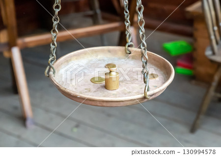 weight and gold coin on brass scales on a chain, scales close-up 130994578