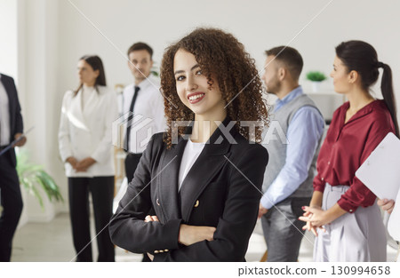 Portrait Of A Happy Curly-Haired Businesswoman With Team In Office Portrait Of A Happy Curly-Haired Businesswoman With Team In Office 130994658