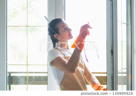 Woman in rubber gloves and apron manually washes window balcony of house with rag cleaner and mop inside interior. Restoring order and cleanliness in spring, cleaning servise Woman in rubber gloves and apron manually washes window balcony of house with rag cleaner and mop inside interior. Restoring order and cleanliness in spring, cleaning servise 130994928