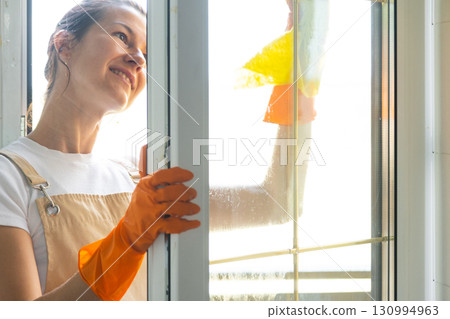 Woman in rubber gloves and apron manually washes window balcony of house with rag cleaner and mop outside behind glass. Restoring order and cleanliness in spring, cleaning servise Woman in rubber gloves and apron manually washes window balcony of house with rag cleaner and mop outside behind glass. Restoring order and cleanliness in spring, cleaning servise 130994963