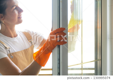 Woman in rubber gloves and apron manually washes window balcony of house with rag cleaner and mop outside behind glass. Restoring order and cleanliness in spring, cleaning servise Woman in rubber gloves and apron manually washes window balcony of house with rag cleaner and mop outside behind glass. Restoring order and cleanliness in spring, cleaning servise 130995074